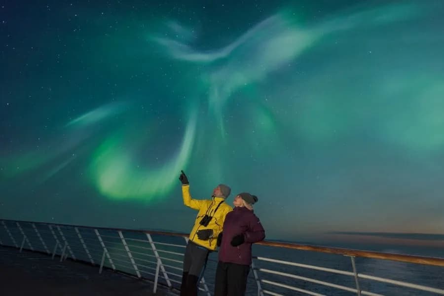 Ship passengers outside observing the northern lights on deck
