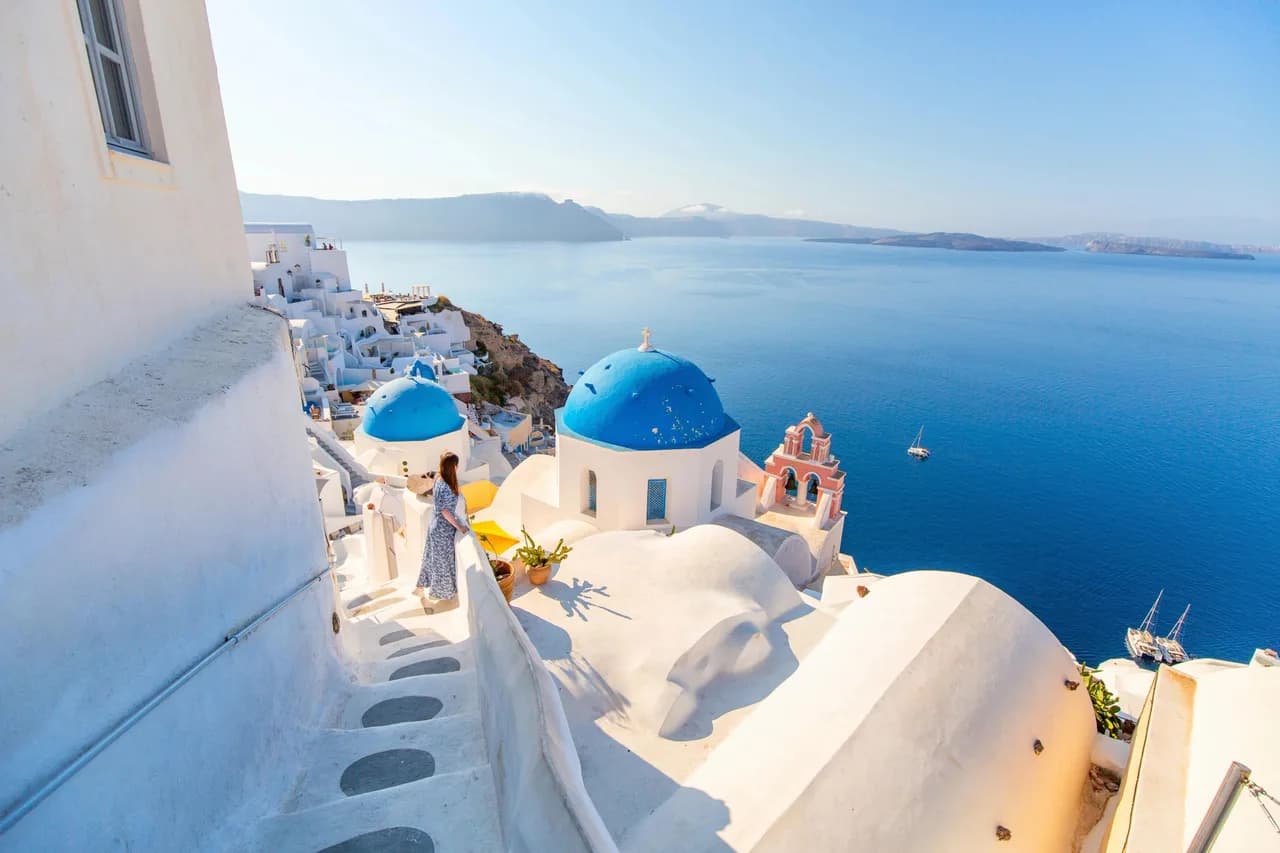 Santorini woman viewing iconic whitewashed cliffside houses framing deep blue Mediterranean waters.