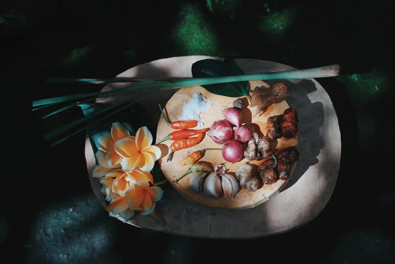 Balinese spices and aromatics including chili, garlic, and shallots filling a rustic wooden tray.