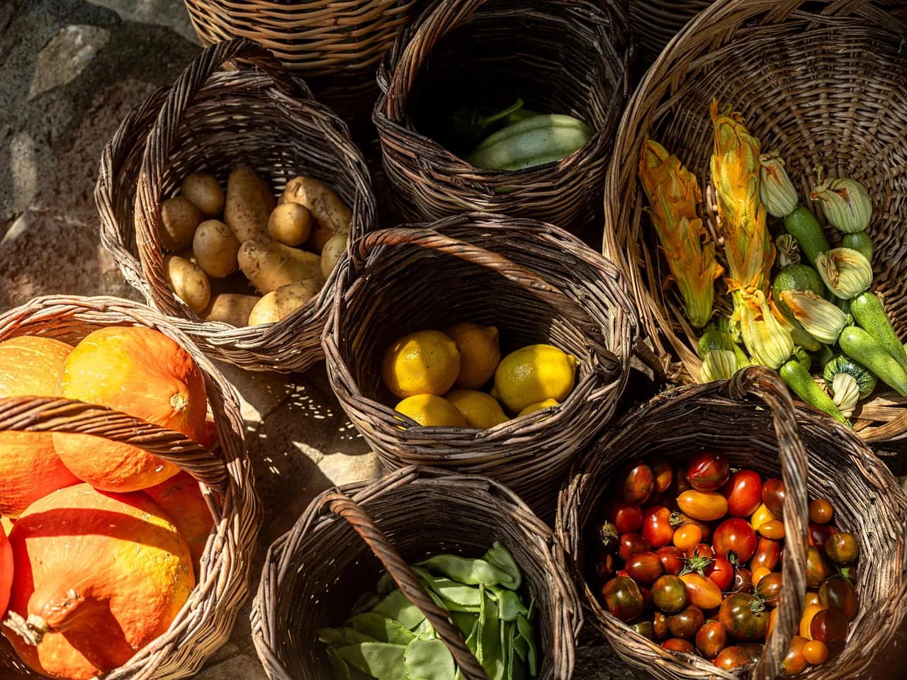 Wicker baskets overflowing with fresh harvest pumpkins, potatoes, lemons, tomatoes, and green beans