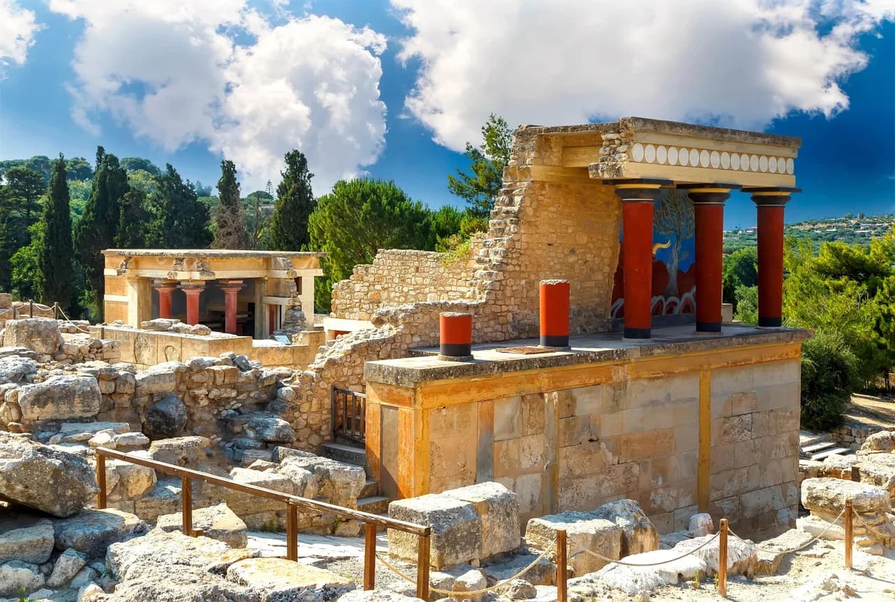 Knossos Palace ancient Minoan ruins displaying distinctive red stone columns under bright blue skies.