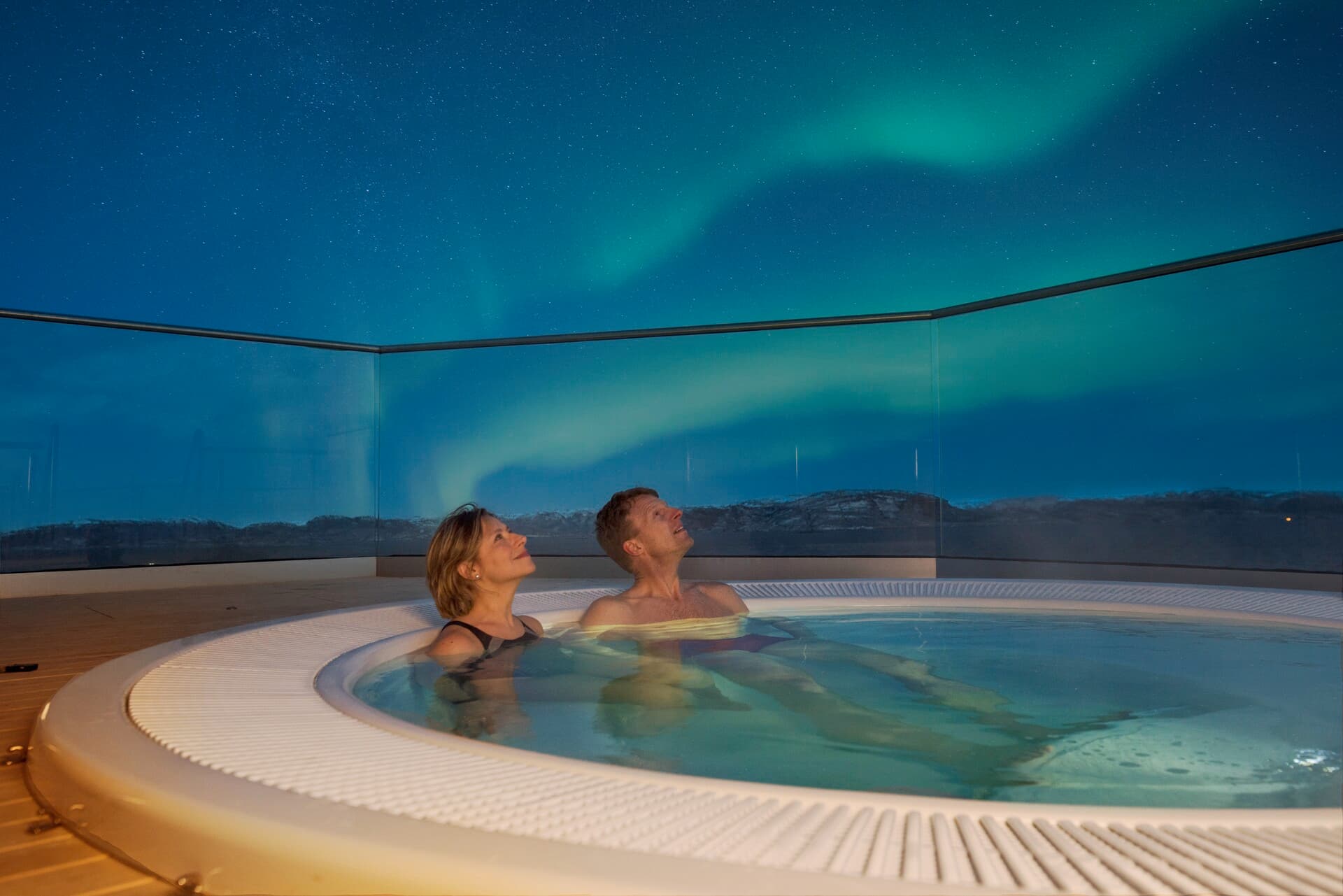Northern Lights above a hot tub on deck on a Hurtigruten cruise in Norway