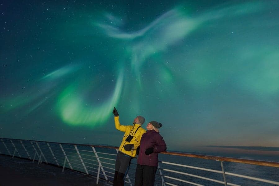 Ship passengers outside observing the northern lights on deck